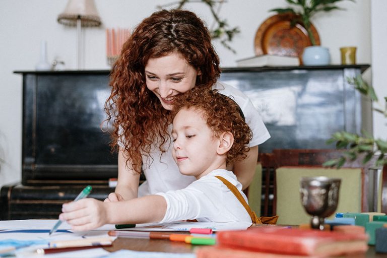 Mother and son spending time together with activity and coloring books at a table.