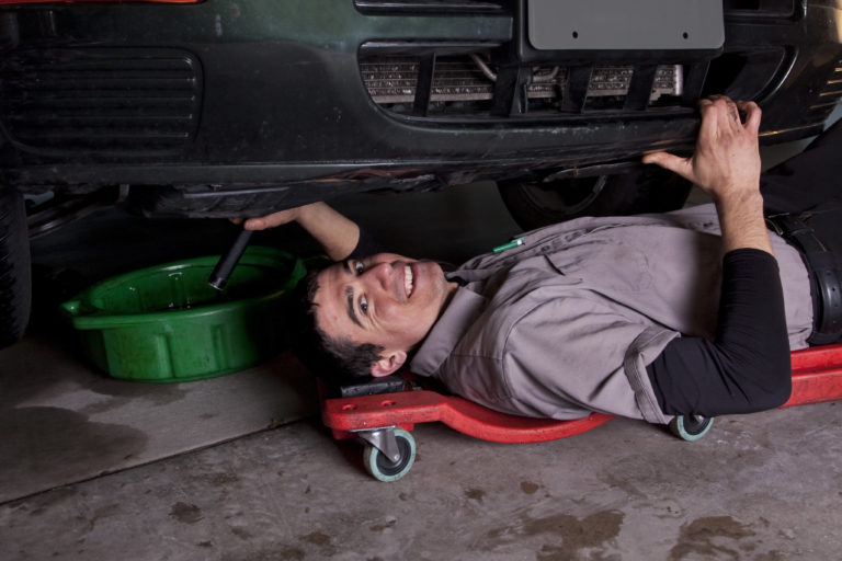 An auto mechanic working under a car doing an oil change