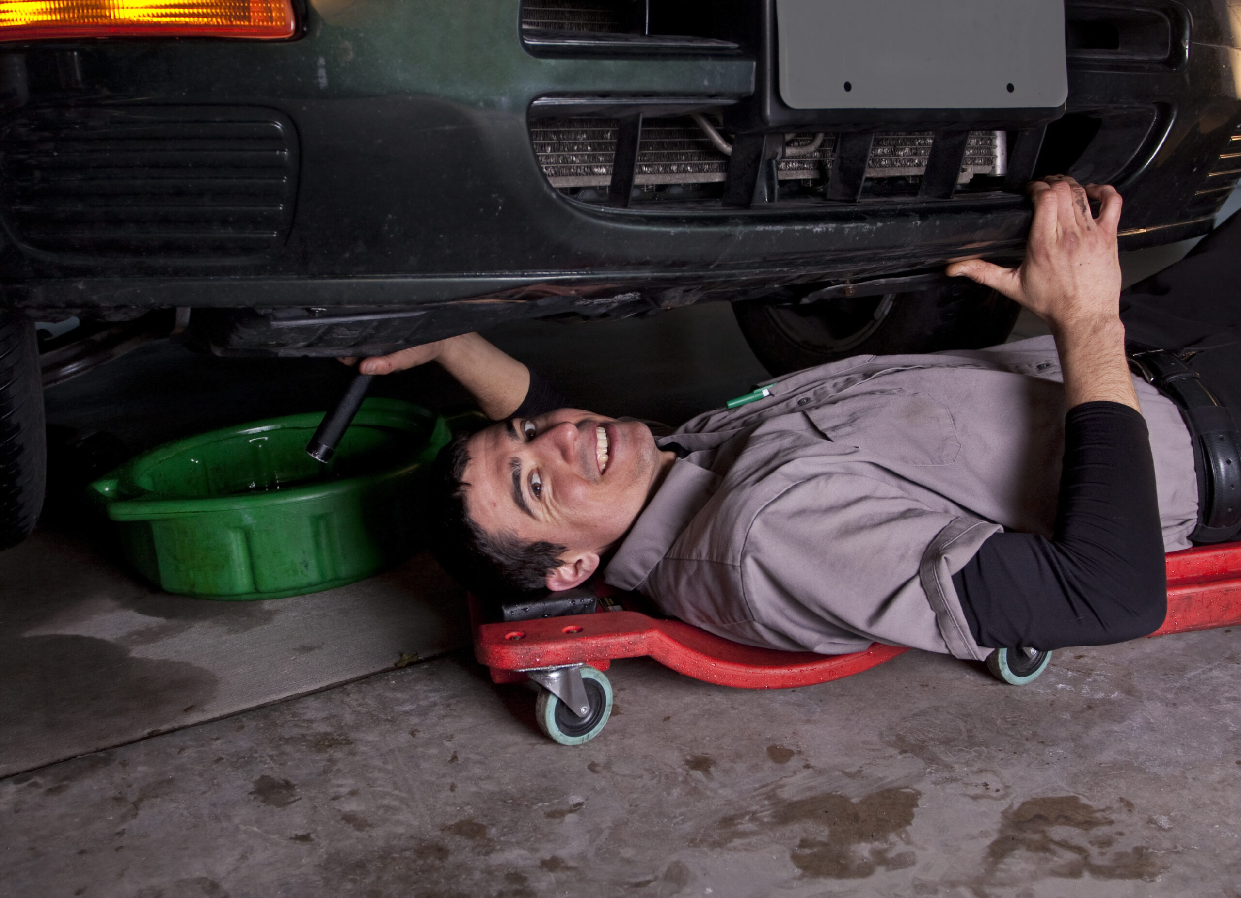 An auto mechanic working under a car doing an oil change