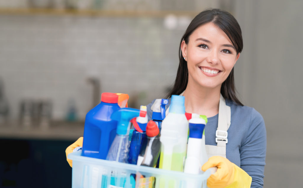 Portrait of a Latin American cleaning woman at home holding cleansing products and looking at the camera smiling